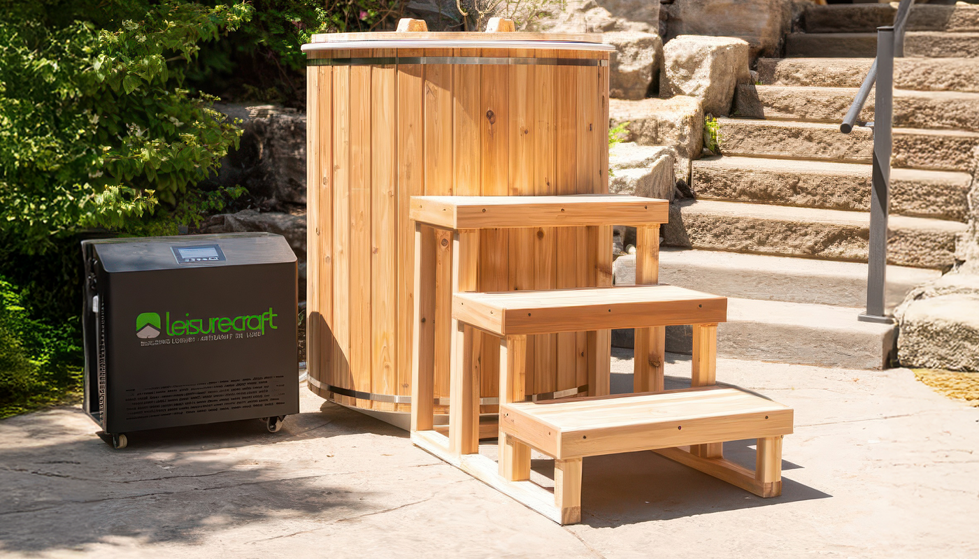 A round wooden cold plunge tub with matching wooden steps and a black Leisurecraft water chiller on a stone patio outdoors.