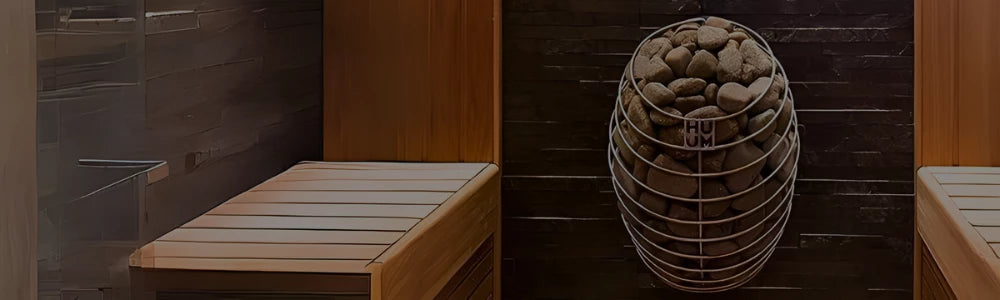 An oval-shaped HUUM sauna heater filled with stones mounted on a dark stone wall next to wooden benches.