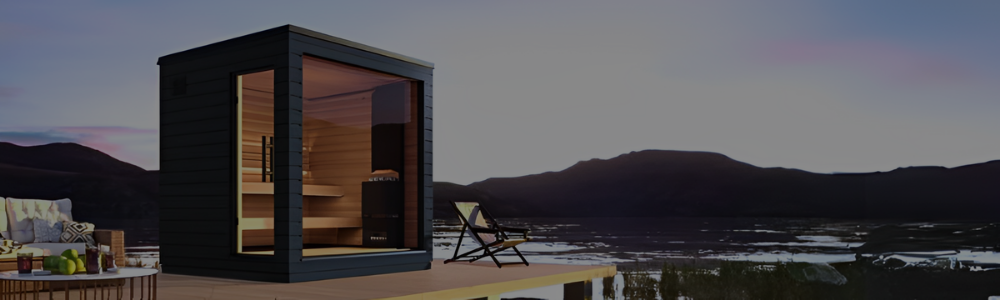 Alt Text: A modern black SaunaLife cube sauna on a deck overlooking a mountain lake at dusk.