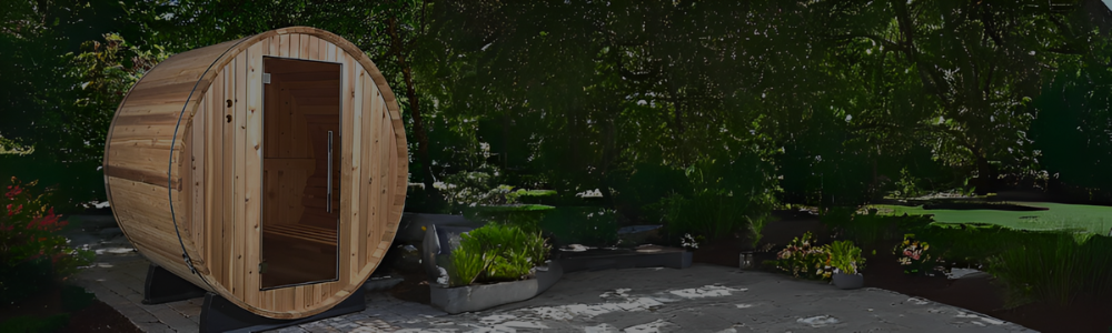 An outdoor wooden barrel sauna with a glass door on a stone patio surrounded by trees.