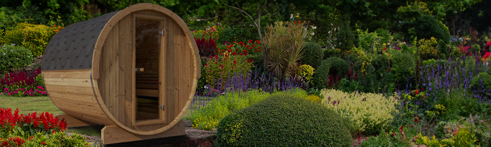 A SaunaLife wooden barrel sauna with a glass door situated in a lush garden filled with colorful flowers and bushes.
