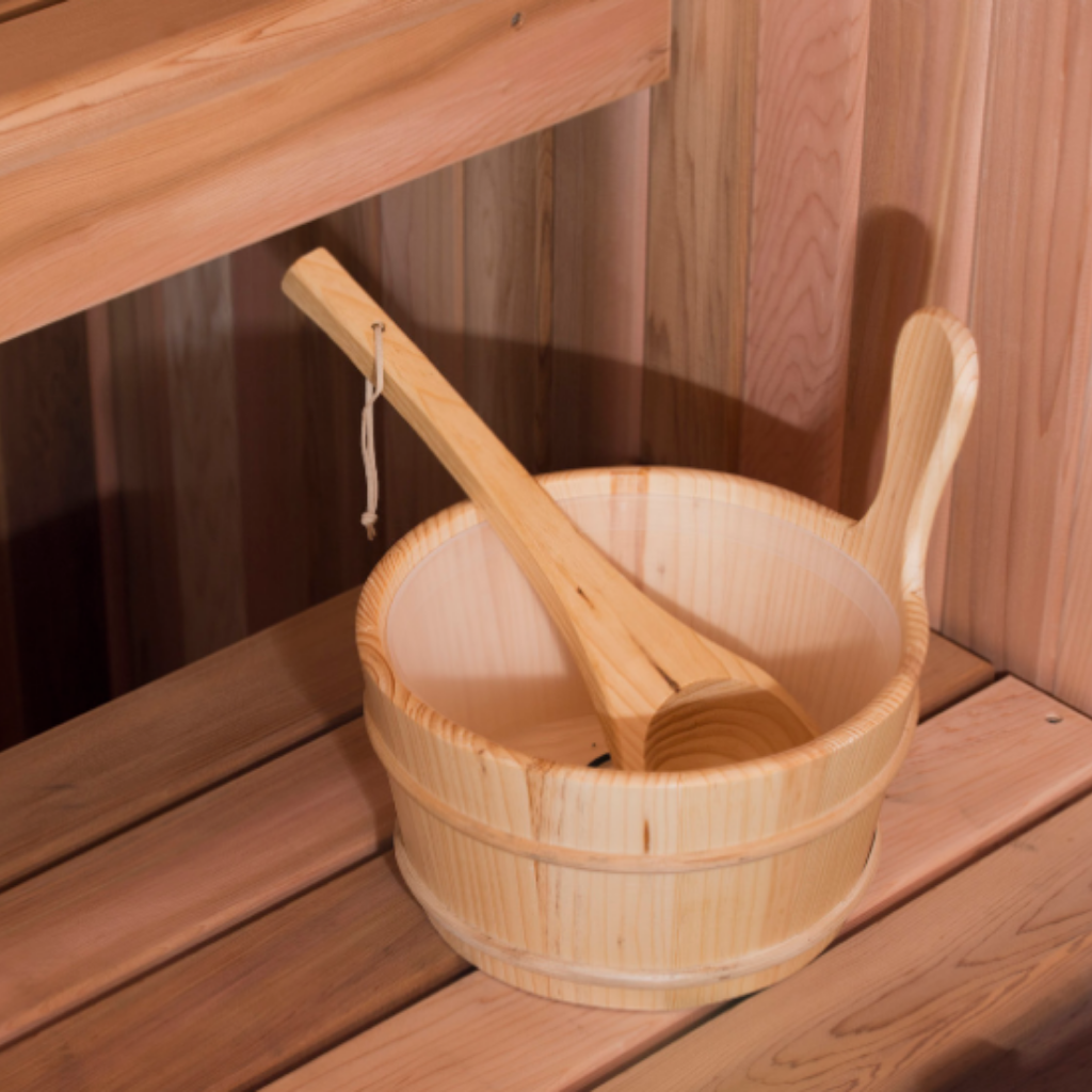 A wooden sauna bucket and ladle sitting on a wooden sauna bench.
