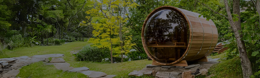 An outdoor wooden barrel sauna with a panoramic glass back window on a grassy hill.