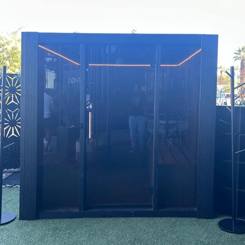 Modern outdoor sauna featuring dark wood siding, tinted glass doors, and interior LED lighting.