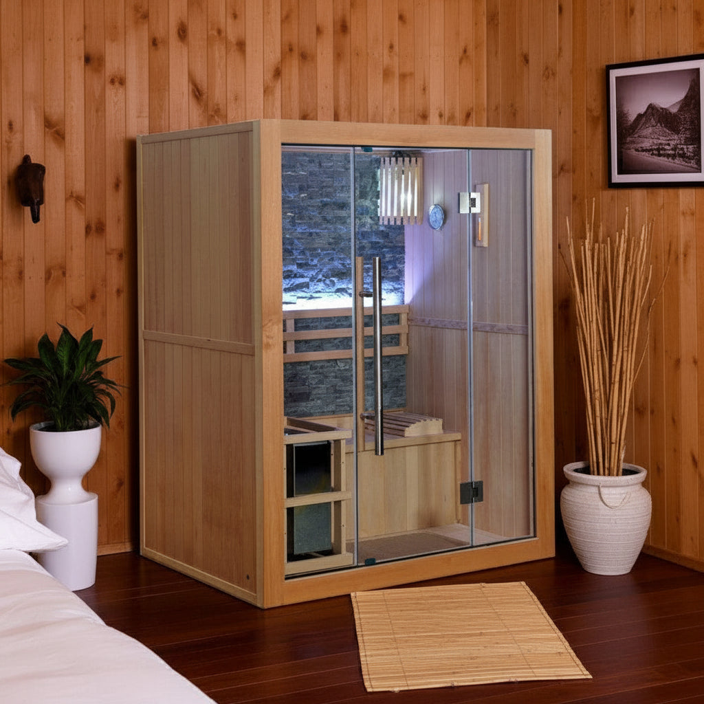 A wooden freestanding sauna cabin with glass doors and interior wooden benches, shown in a wood-paneled bedroom or spa room setting with a bed corner, plant, vase, wall art, and mat on the floor.