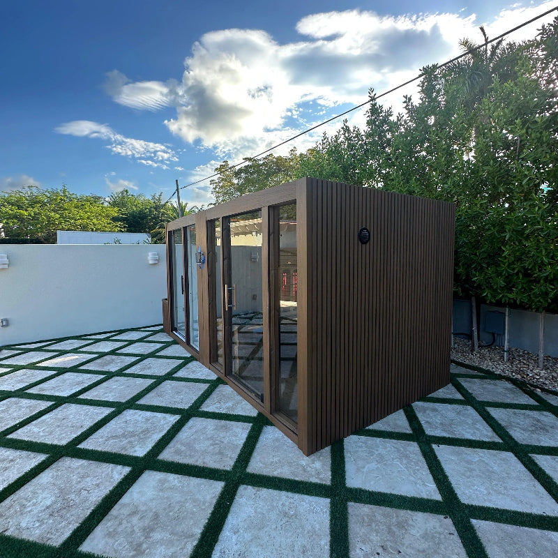 Modern outdoor shed with glass doors on a patio with green and gray tiles.
