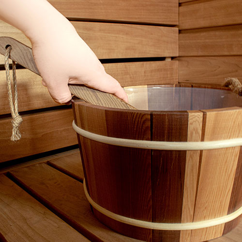 Wooden bucket with a hand lifting the lid in a wooden sauna setting