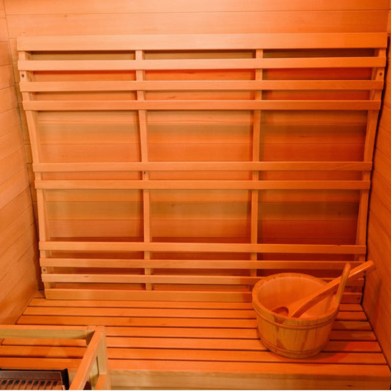 A wooden sauna interior with tiered slatted benches, a hanging wooden bucket, and a wooden paddle inside, shown under warm orange lighting.