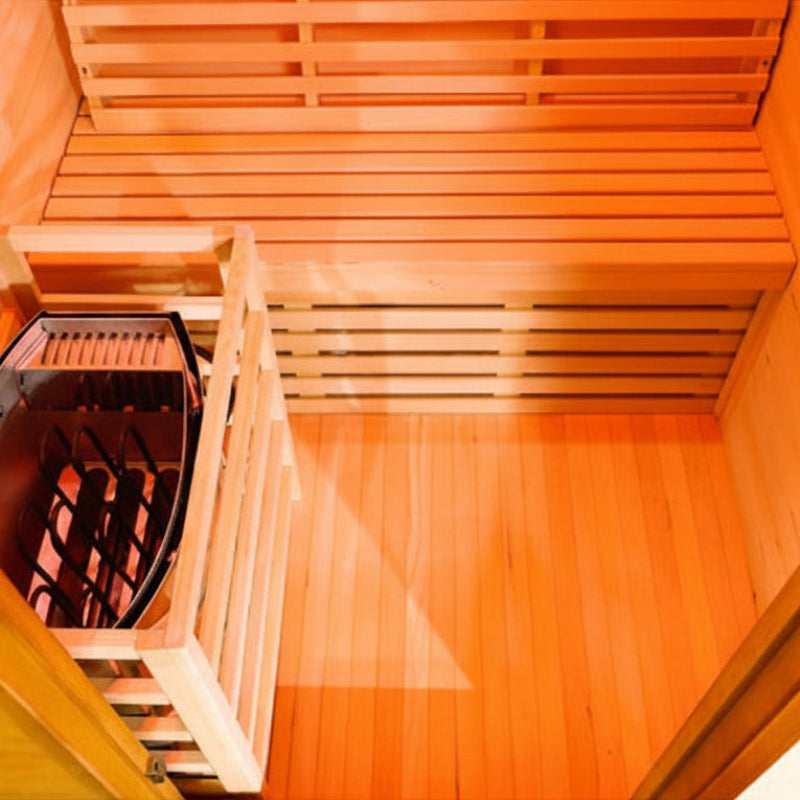 An overhead view of a wooden sauna interior with tiered wooden benches and a dark metal infrared sauna box on the left, shown against a white background.