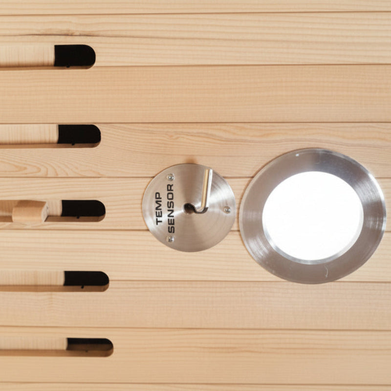 A close-up of a light natural wood slatted surface with several small rectangular cutouts containing black and beige elements, plus a round silver metal sensor plate and a circular opening.