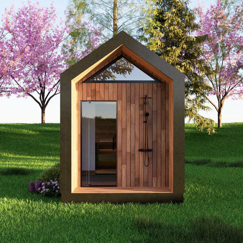 A small modern wooden cabin with a pitched roof, wood-paneled front wall, large glass door, and built-in shower fixture, shown on a grassy lawn with flowering trees in the background.