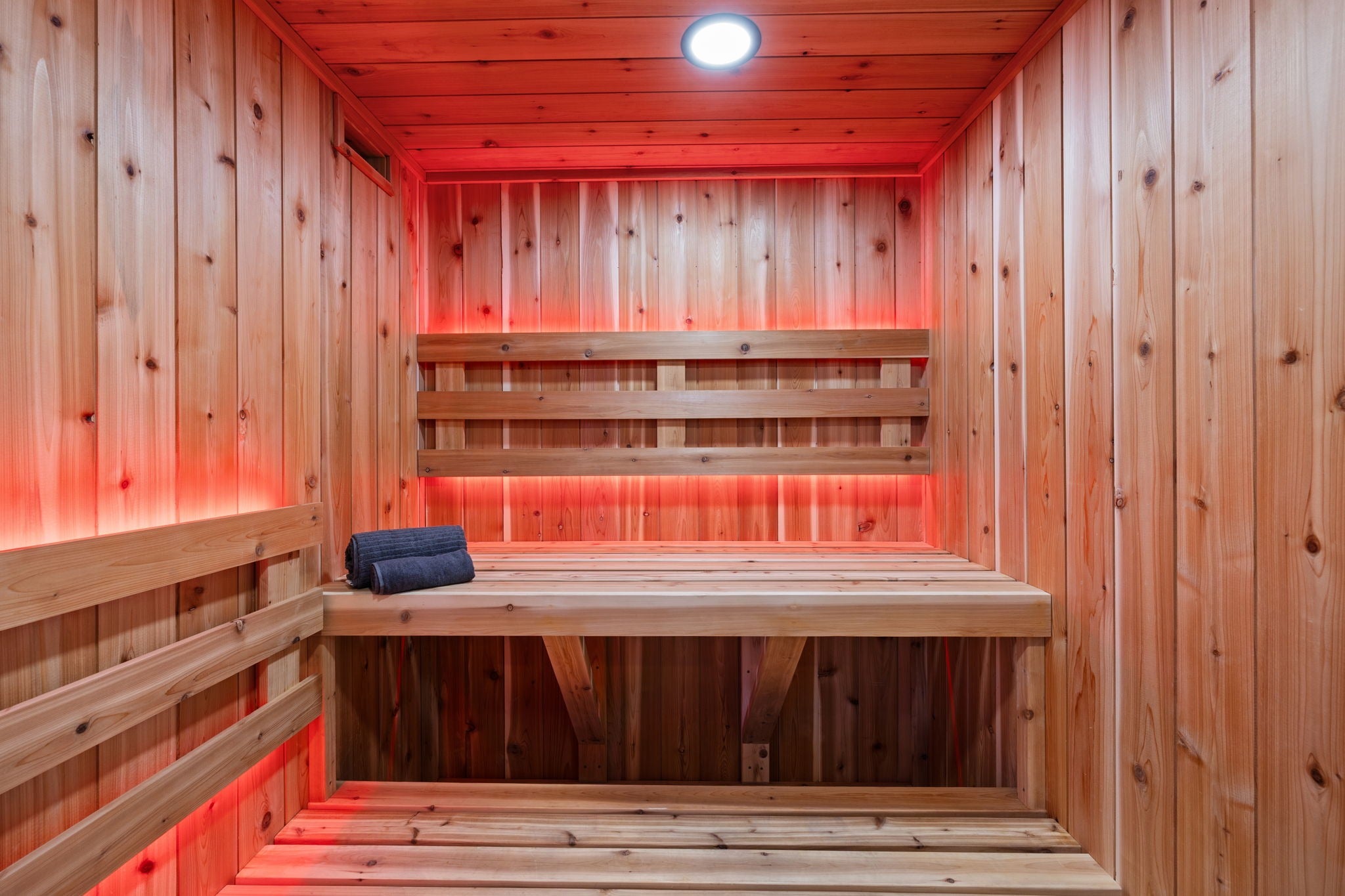 Wooden sauna with red interior lighting and wooden benches.
